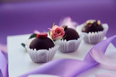 Şenlikli çikolata şekerlemeleri. Narin pembe tüyler ve mor kurdele. Mor renk düzeni arkaplanı.