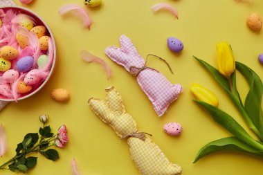 Paskalya Bayramı kartpostalı konsepti. Renkli yumurtalı pembe kase, pembe tüyler, çiçekler ve el yapımı sevimli tavşanlar.