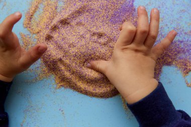 Çocuk elleri renkli kumlarla oynar. Üst Manzara. Çocukların motor becerileri gelişiyor. Yaratıcı çocuk mesleği