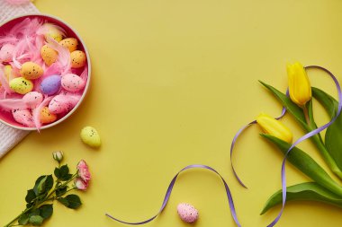 Paskalya 'nın parlak geçmişi. Renkli yumurtalı pembe kase, pembe tüyler, bahar çiçekleri. Mutlu Paskalyalar. Kopya alanı olan kartpostal.