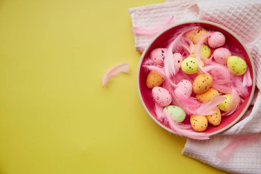 Minimalist Paskalya yumurtaları pembe kasede, sarı arka planda pembe tüylerle. Metin için yer