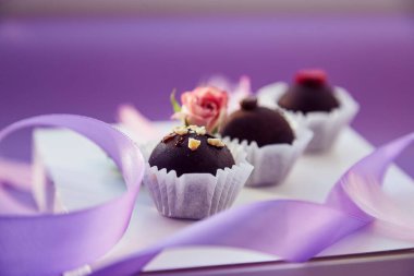 Zarif çikolata şekerlemeleri. Pembe tüyler, pembe gül ve mor kurdele. Mor renk düzeni arkaplanı.