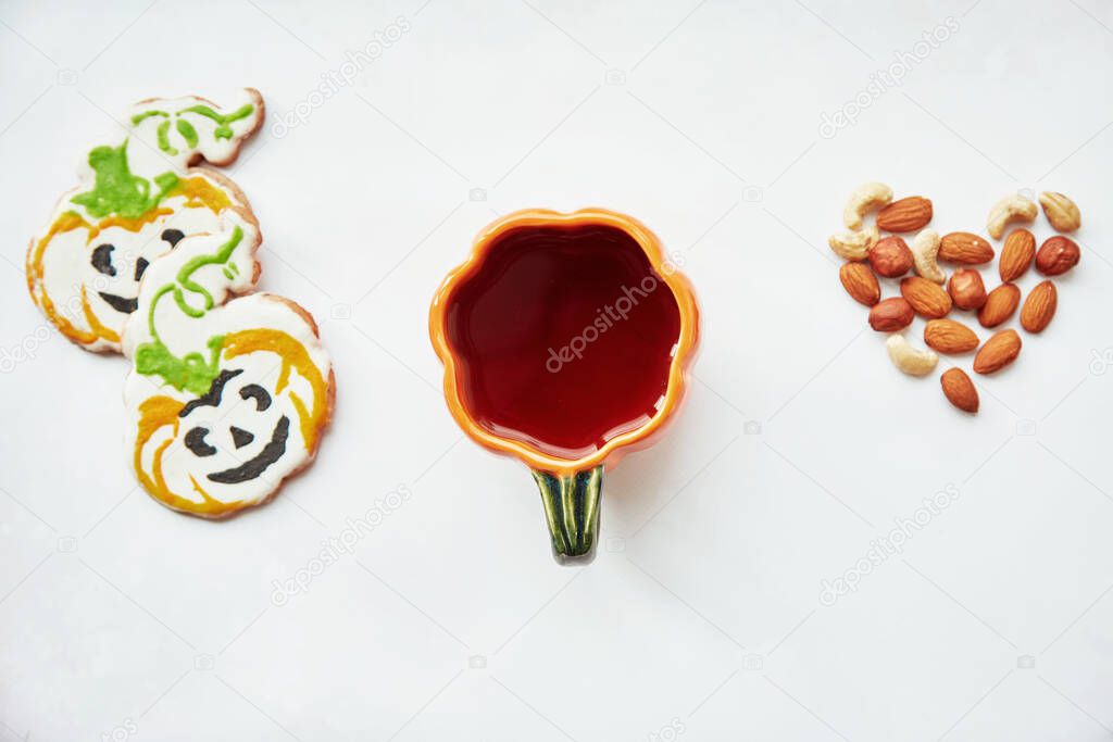 Halloween creative background: pumpkin cup and homemade cookies in shape of cute pumpkins and almonds heart. Trick or treat concept. Aesthetic autumn coziness mood. Autumn decorations. Copy space
