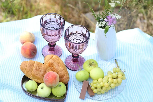 Romantic summer picnic: croissants, fruits, chocolate, grapes and glasses of wine on blanket. Cottage core aesthetic. Summer vibe