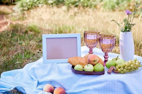 Summer picnic with croissants, fruits, chocolate and glass of wine in the evening forest. Mock up frame, place for your text. Cottage core aesthetic. Summer vibe