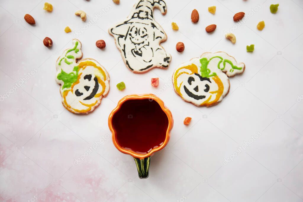 Halloween creative concept: pumpkin cup and homemade cookies in shape of cute pumpkins and ghost closeup. Aesthetic autumn mood or trick or treat concept. Autumn cozy home concept