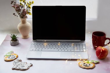 Cadılar Bayramı 'nda ev ofisin sıcacık olsun. Bilgisayarı, kırmızı bardağı ve balkabağı şeklinde ev yapımı kurabiyeleri hazırla. Çelenklerle dolu rahat bir atmosfer. Boşluğu kopyala