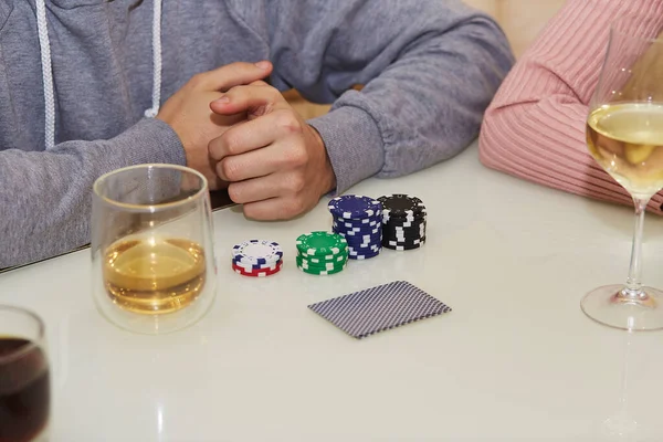 Player\'s hands in poker on the white table in gambling game. Glasess of champagne and whiskey. Candid moment. Poker background lifestyle photography. Enjoying the moment, digital detox with friends