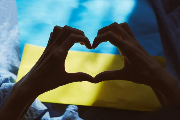 Heart shaped hands on Ukrainian flag with shadows. Priority question. Breaking news. Ukrainian flag, Creative patriotic background. Stop the war in Ukraine. Stop Russian aggression