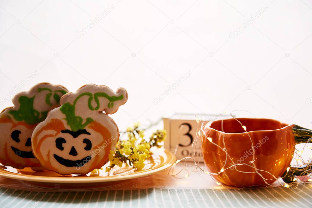 Happy Halloween still life with pumpkin cup and homemade cookies in shape of cute pumpkins and date of Halloween Day. Atmospheric aesthetic autumn holiday concept. Rural life. High quality photo