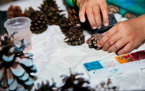 Bir çocuğun yılbaşı konilerini renklendirmesi. Çocuklara öğretmek, motor becerilerini geliştirmek. Küresel el işi hobisi. Noel için hazırlanıyorum. Doğal süsler. Yüksek kalite fotoğraf