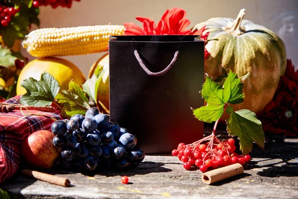 Autumn creative mock up of gift bag among fruits and vegetables, pumpkin, corn, pears, grapes, viburnum and melon. Thanksgiving Day concept. Autumn aesthetic still life with trendy natural shadows.