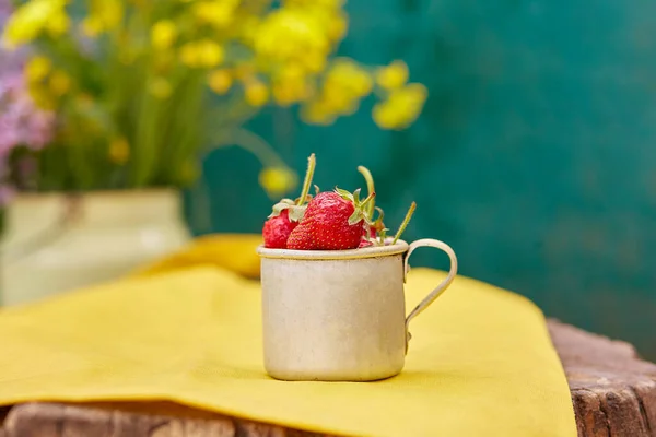 Strawberries in a metal aluminum travel mug on wooden stump. Natural green and yellow spring background. Cottagecore aesthetics concept, trendy shadows background. Copy space. High quality photo