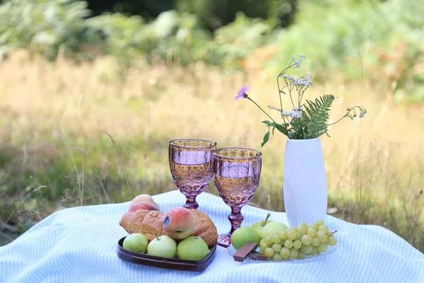 Summer picnic with croissants, fruits, chocolate and glass of wine in the forest. Cottage core aesthetic. Summer vibe