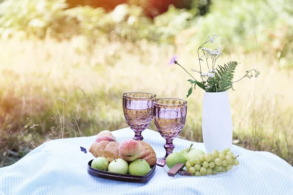 Romantic summer picnic with croissants, fruits, chocolate, grapes and glasses of wine in the forest. Cottage core aesthetic. Summer vibe