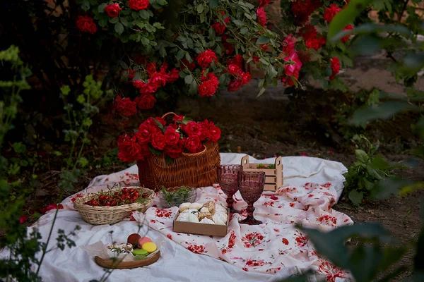 Masa örtüsü marşmelovlu, bezelyeli, çilekli, çilekli, şarap kadehli, bahçedeki pembe güllerin arasında kirazlı estetik pembe piknik. Romantik yemek..