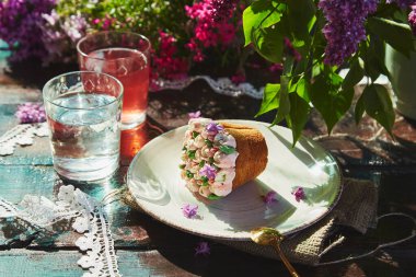 Taze komposto, bir bardak su, şenlikli kek, çiçekler ve dantel süslemeyle yaz bahçesi kahvaltısı. Parlak yaz renkleriyle güneşli bir günde kır evi pikniği. Sert gölgeler.