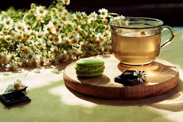 Aesthetic summertime tea time, herbal tea and macarons dessert outside in the terrace under trendy hard shadows. Sweet desserts, natural chamomile herbal tea - natural sustainable eco-friendly lifestyle.