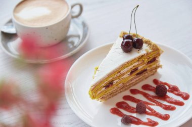Kirazlı, ahududulu bisküvili kek, dışarıdaki ahşap masada bir fincan kapuçino. Kafe terasında pembe çiçek süslemeleri. Şeker yok, doğal tatlılar..
