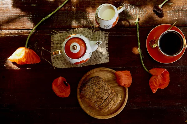 Traditional poppy seed bun with cup of tea and milk near poppies flowers and dishes with poppies ornaments. Delicious breakfast in summer. Lifestyle photography