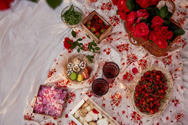 Summer aesthetic pink picnic with tablecloth marshmallows, macaroons, peas, strawberries, glasses of wine, cherries among pink roses in the garden. Romantic dinner.