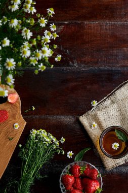 Fresh strawberries, summer chamomile flowers, herbal tea and mint on wooden table. Atmospheric feminine summer lifestyle. Beautiful food. Flat lay food. Copy space