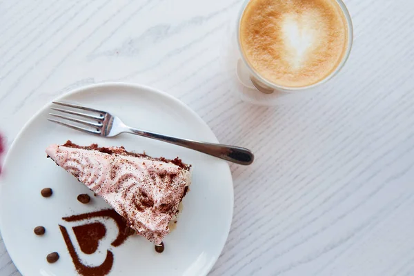 Fruit chocolate cake and a glass with a double bottom of latte on wooden table outside in the cafe terrace. Atmospheric breakfast. Heart shaped dessert decorations