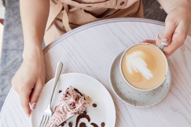 Kadın elleri kahve terasındaki ahşap masada meyveli kapuçino ve kek tutuyor. Atmosferik kahve zamanı. Kalp şeklinde tatlı süslemeleri.