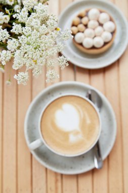 Tender hazelnut tart and cappuccino in white ceramic cup on wooden table at the terrace background. Selective focus. Aesthetic breakfast on cold autumn weather. Flat lay food.