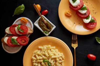 Fusilli pasta, caprese salad with tomato, basil, mozzarella with pesto in low key. Bread appetizer with caprese salad. View from above. Italian dinner
