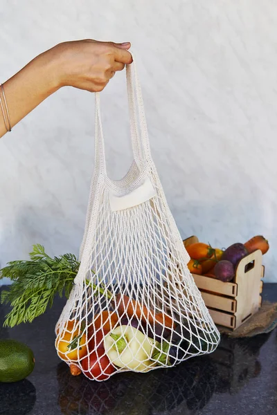 Woman holds eco shopping reusable bag full of fresh vegetables - tomatoes, purple potatoes, carrots, sweet pepper. Ecological concern, eco shopping. Vegan eco-friendly lifestyle.