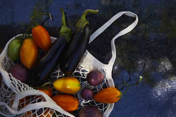 Harvest vegetables in eco shopping bag with colorful tomatoes, eggplants, purple potatoes, under trendy hard shadows with reflection background. Ecological concern. Copy space