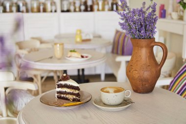 Çikolatalı kek ve kafedeki ahşap masada bir fincan kapuçino. Lavander sürahide. Estetik kahve zamanı. Kendine zaman ayır.