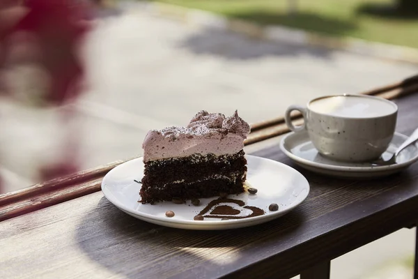 Atmosperic natural piece of cake and a glass of cappuccino on wooden table outdoor in the cafe terrace. Aesthetic coffee time. Time for yourself. Hard shadows.