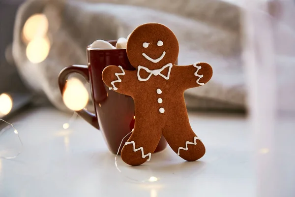 Homemade gingerbread cookie and blurred bokeh background close up. Festive Christmas decorations with hot drink and marshmallows. Aesthetic Christmas atmosphere, home coziness, warmth concept