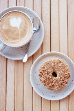 Terastaki ahşap masada beyaz seramik bardakta şekersiz çörek ve kapuçino. Estetik kahvaltı