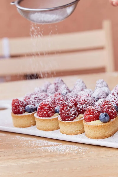 Dressing of French traditional blueberry and raspberry tartlets of sprinkled with powder outside. Aesthetic food.