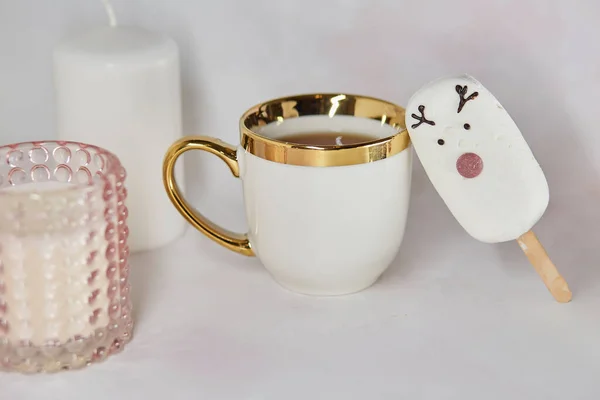 Festive afternoon tea with white cup, cute marshmallow deer, gingerbread cookie and pink candle. Aesthetic tea time. Christmas inspiration concept. Good morning or cozy home concept