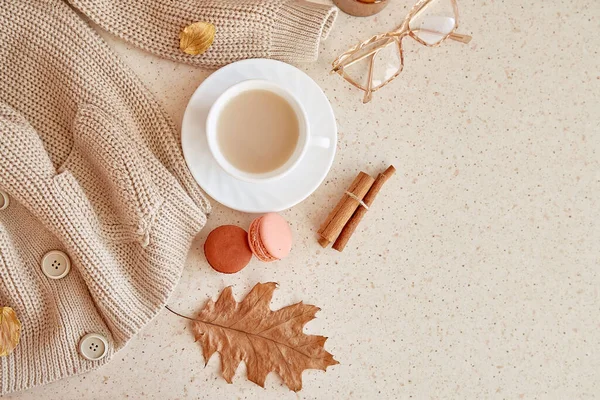 Feminine fall cozy home lifestyle - sweater, glasess. Atmospheric coffee time among oak leaves, cinnamon sticks, macaroons. Copy space