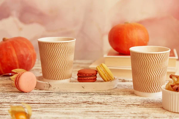 Aesthetics cardboard cups with pumpkin latte. Seasonal couple breakfast with coffee and macaroons among pumpkins. Cozy autumn atmosphere.