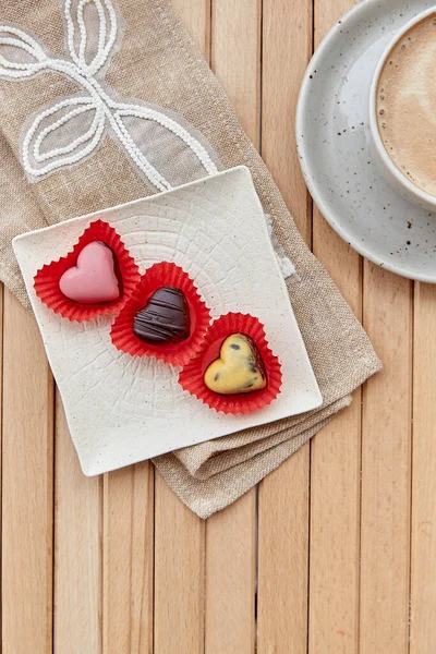Chocolate assorted sweets in shape of hearts and cup of cappuccino. Aesthetic coffee time outside. Romantic date, Valentines day.