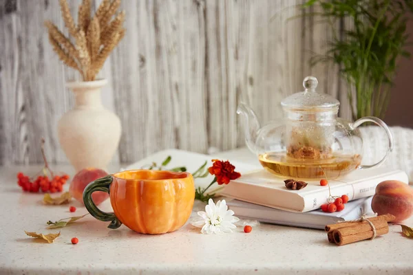 Aesthetic organic linden tea in teapot on the books and cup of tea in shape of pumpkin. Dry fragrant flowers, wheat, autumn arrangements, figs, peaches. Cozy atmosperic relaxing at home