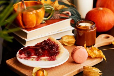 Balkabağı şeklinde bir fincan kahve, kirazlı turta, badem kurabiyesi, balkabağı, sonbahar süslemeleri arasında mum. Ön planda bulanıklık. Hygge rahat ev.
