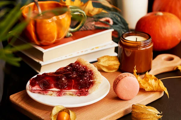 Balkabağı şeklinde bir fincan kahve, kirazlı turta, badem kurabiyesi, balkabağı, sonbahar süslemeleri arasında mum. Ön planda bulanıklık. Hygge rahat ev.