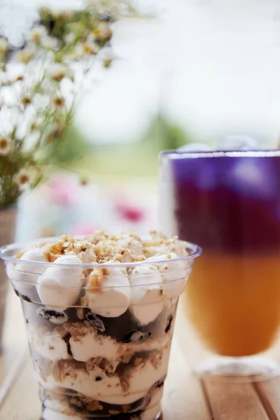 Vegan portion of nuts dessert in a disposable cup. Purple and yellow cocktail - anchan blue tea with antioxidants and nootropics at the terrace near chamomile flowers.