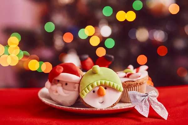 Christmas cupcakes. Decorative cupcakes of creative Santa Claus, snowman in front of the Christmas tree. Good holidays mood. Selective focus