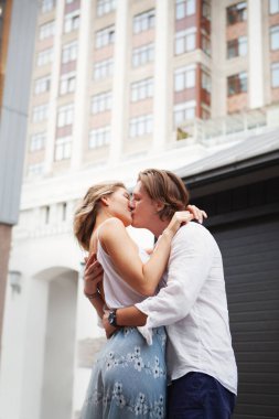 Affectionate young couple kissing and embracing while standing together on city street. Light Vertical portrait of romantic beautiful models. Natural color, lifestyle