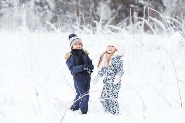 Happy Children playing outdoors in cold winter weather, having fun and throwing snow in the forest. Active family holidays