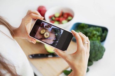 Sosyal medyada paylaşmak için beyaz arka plan masasında taze yeşil salatanın fotoğrafını çeken akıllı telefon kullanan yemek blogcusunun elleri