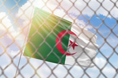 A steel mesh against the background of a blue sky and a flagpole with the flag of algeria